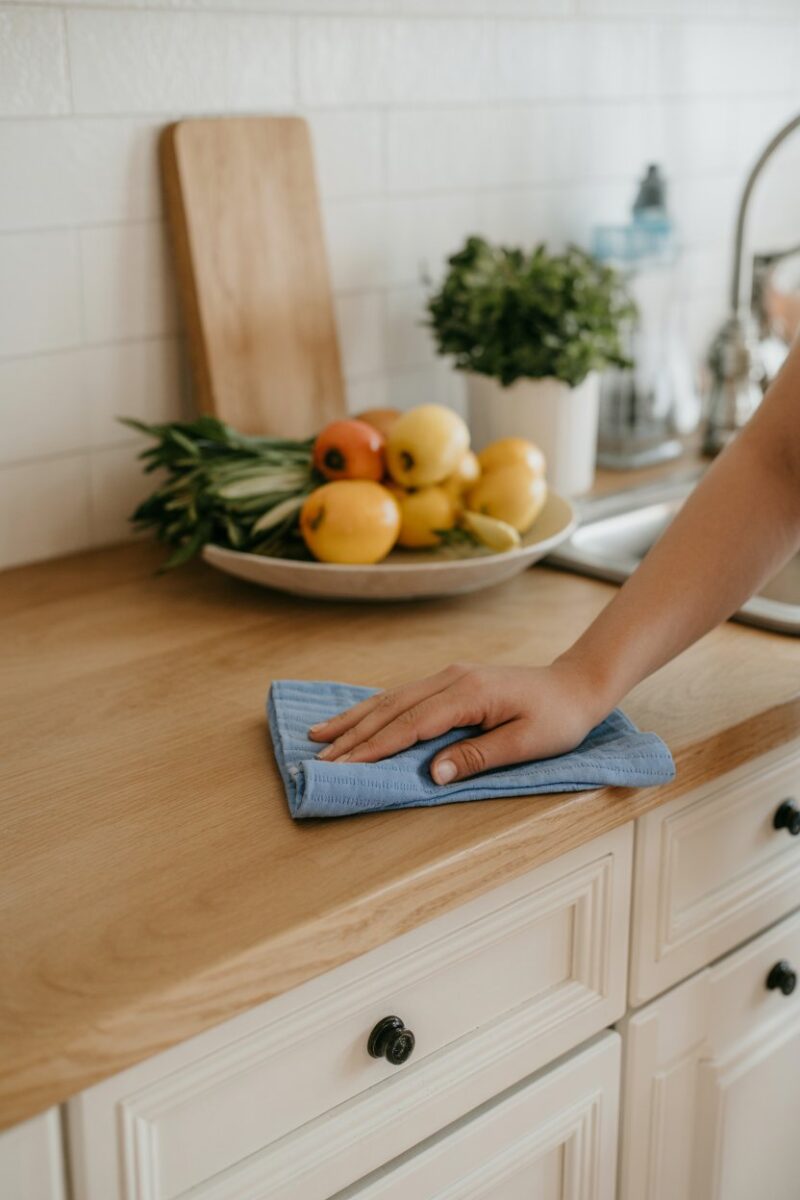 A person wiping down a kitchen counter with a blue cloth.