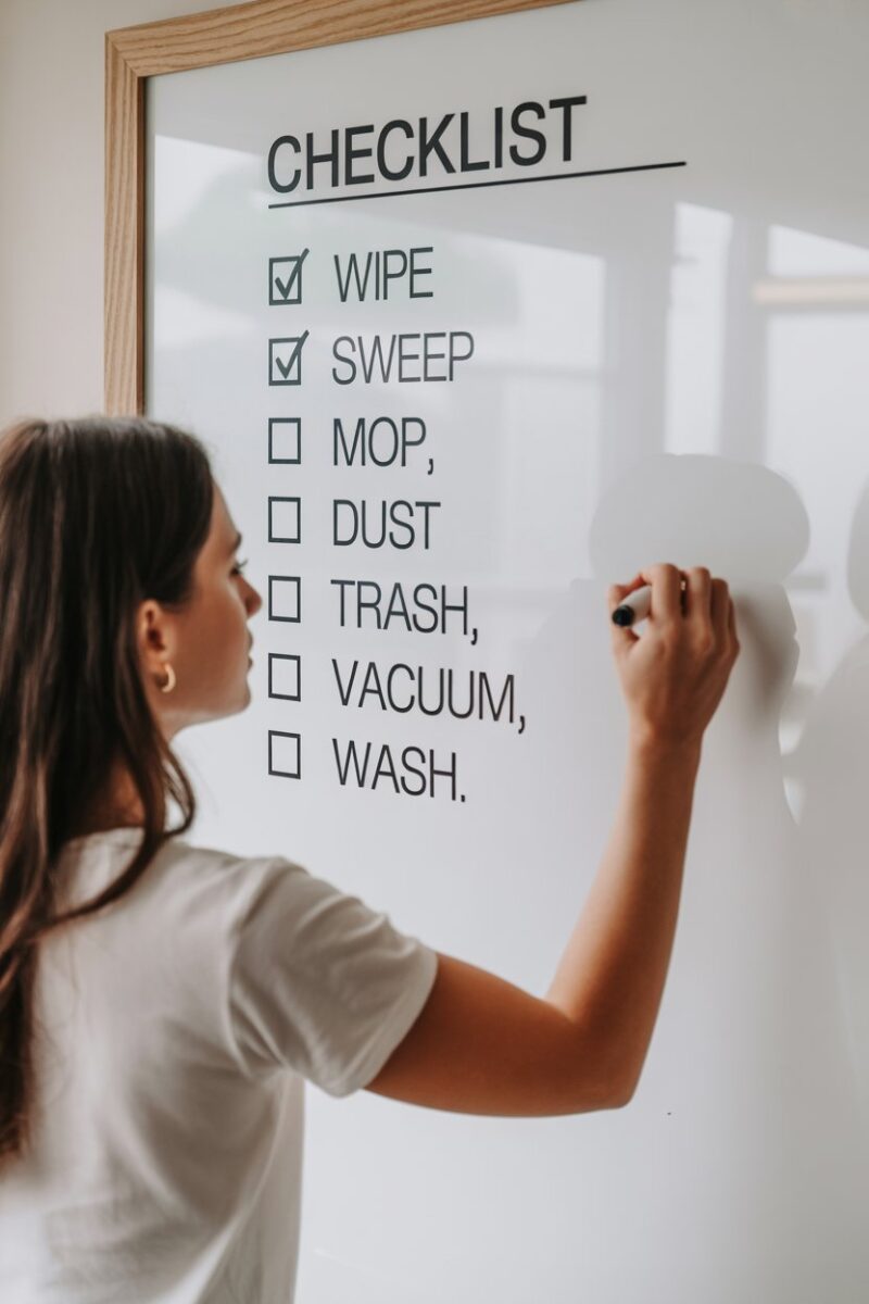 A person writing on a whiteboard with a checklist of cleaning tasks in a bright, organized room.