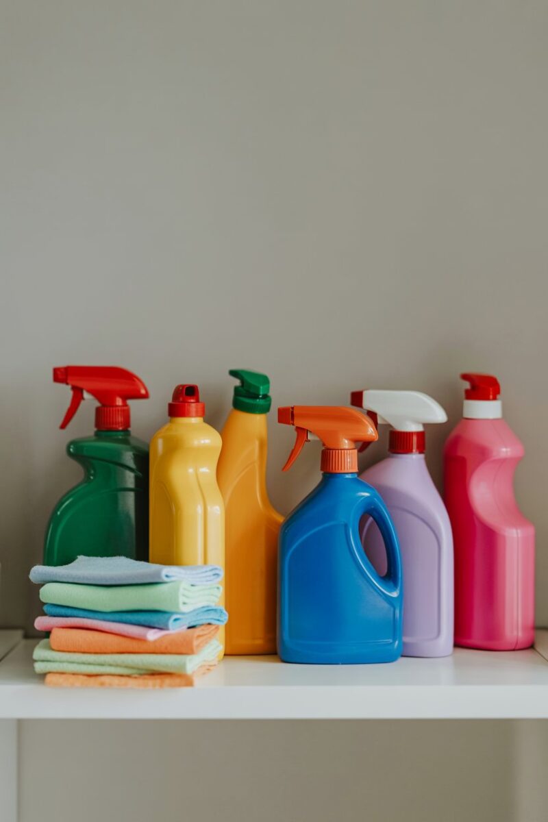 A shelf with various cleaning supplies, including colorful cleaning rags and bottles.