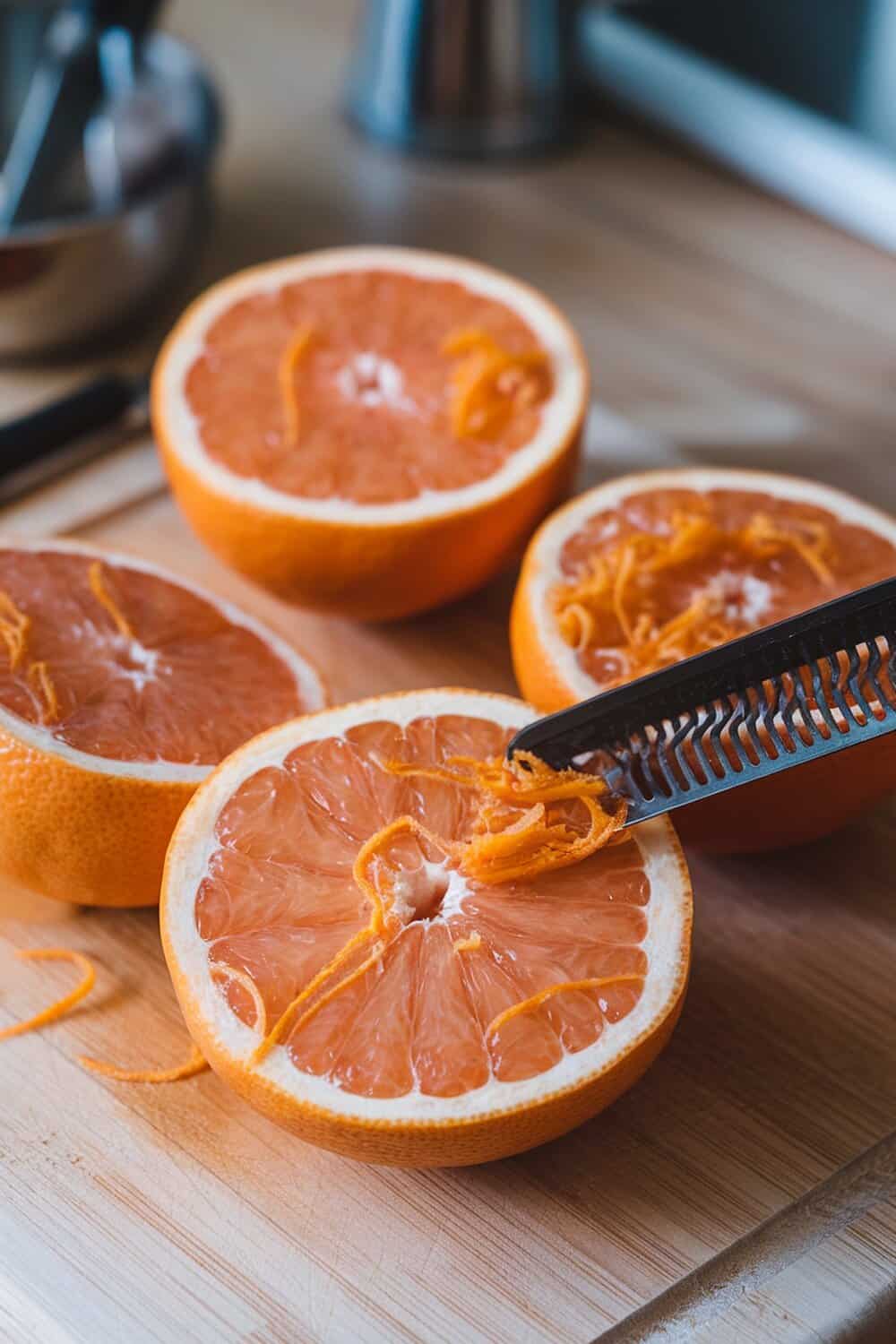 Freshly cut grapefruit halves with zest being scraped out.