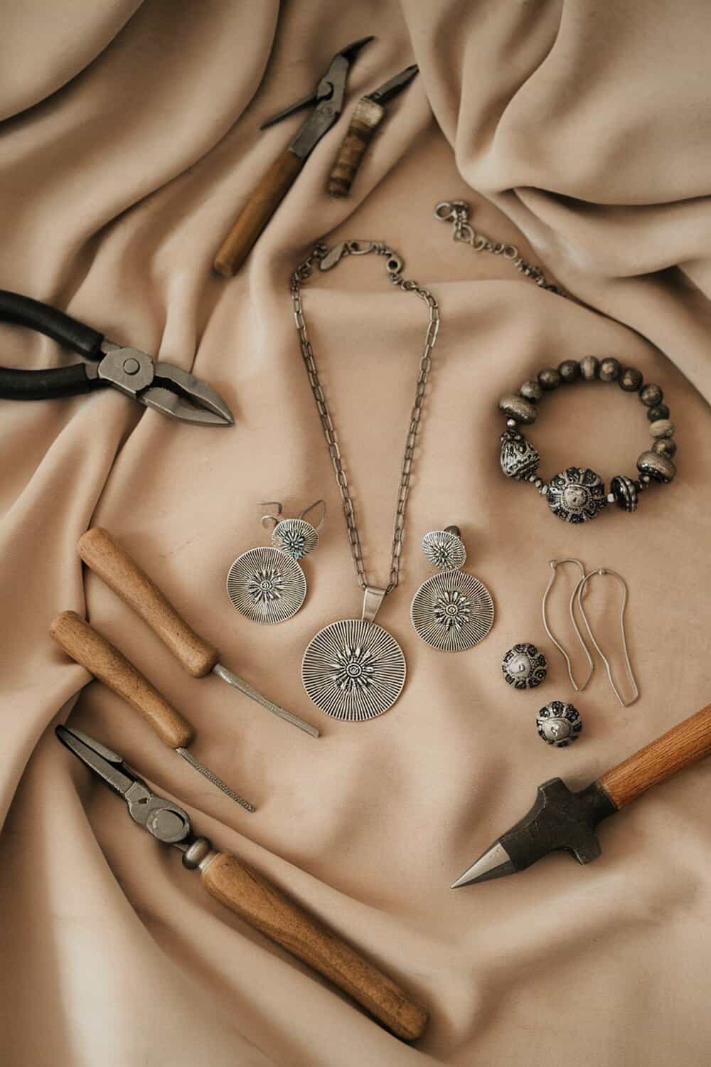 A collection of handmade jewelry pieces and tools on a soft fabric background.