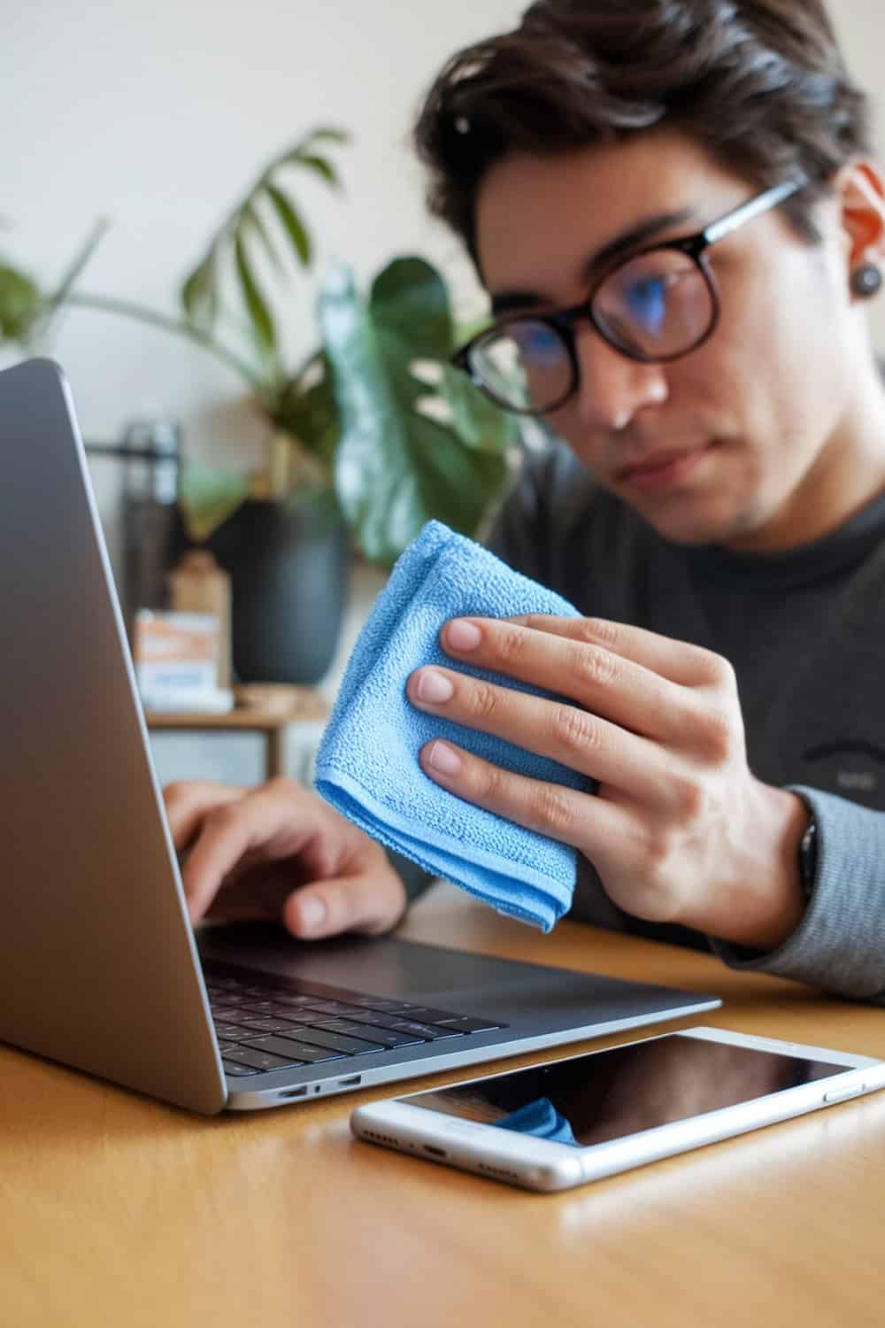 Person cleaning a laptop and phone with a blue microfiber cloth.