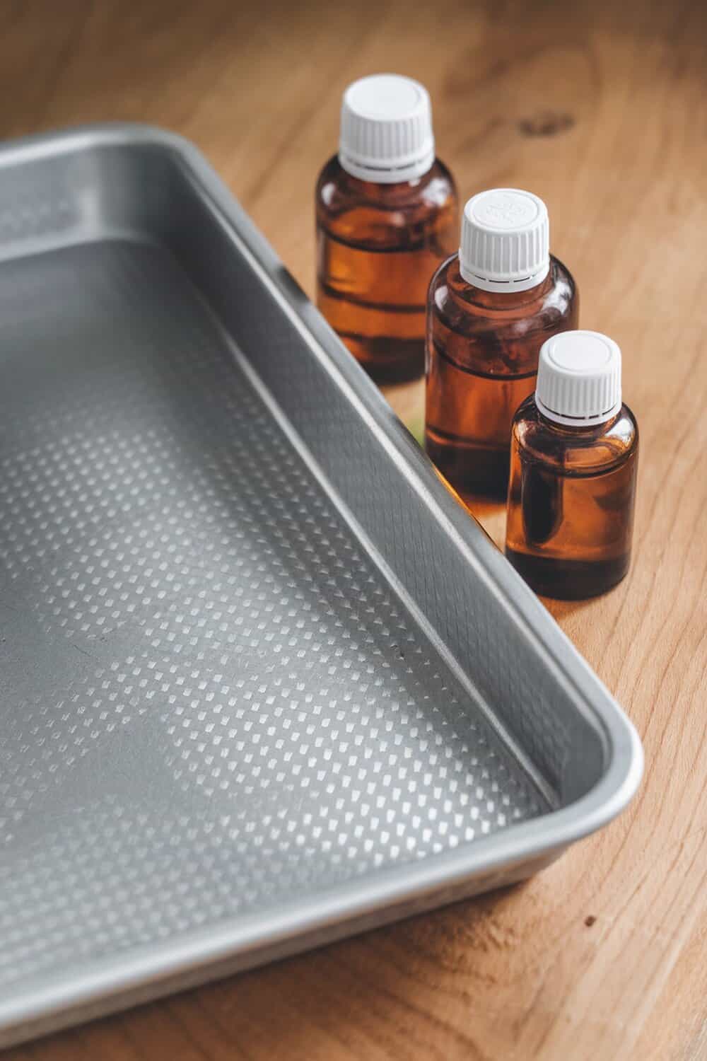 A clean cookie sheet next to bottles of essential oils on a wooden surface.