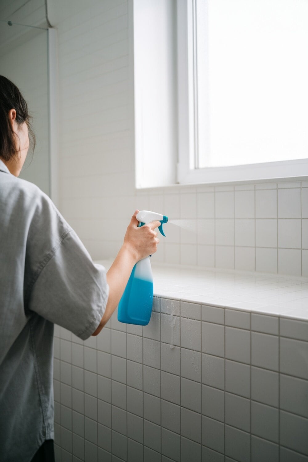 Person cleaning a bathroom surface with a spray bottle.