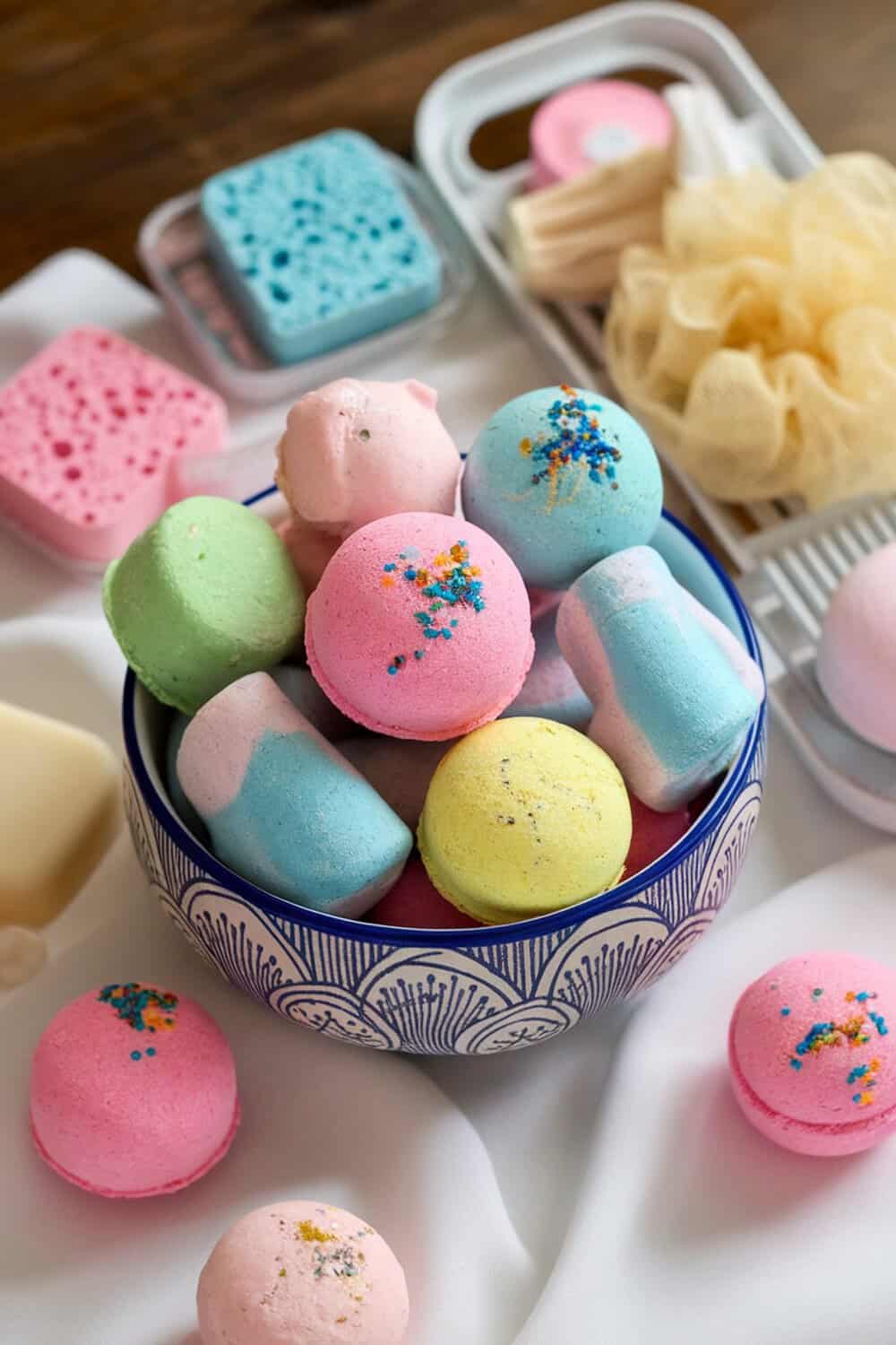 Colorful homemade bath bombs in a bowl with sponges and bath accessories.
