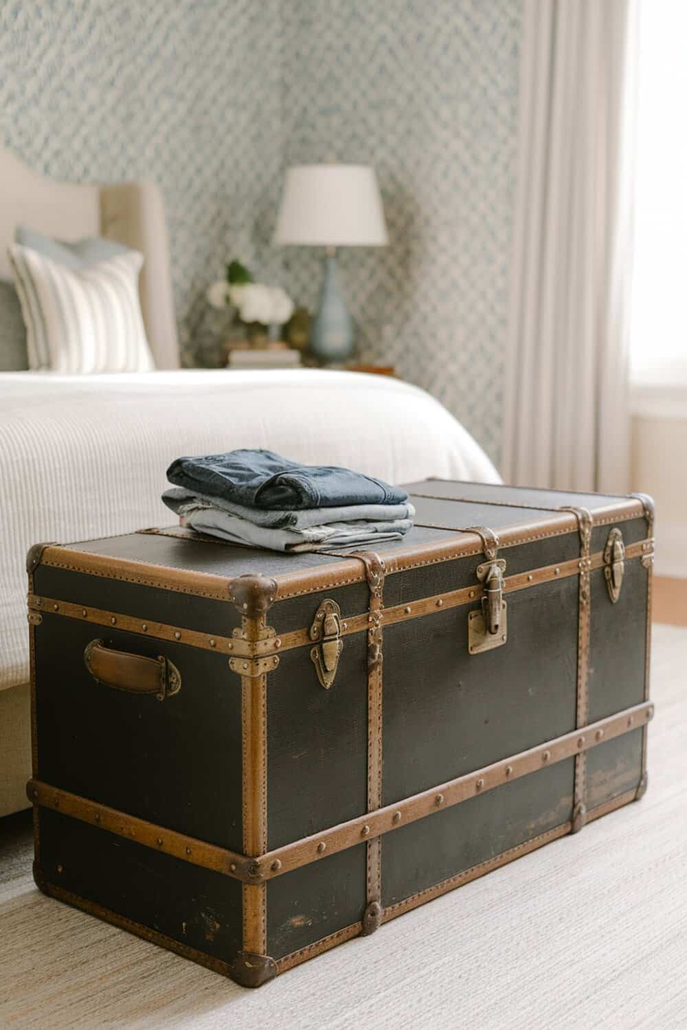 A vintage trunk used for storing clothes, placed at the foot of a bed.