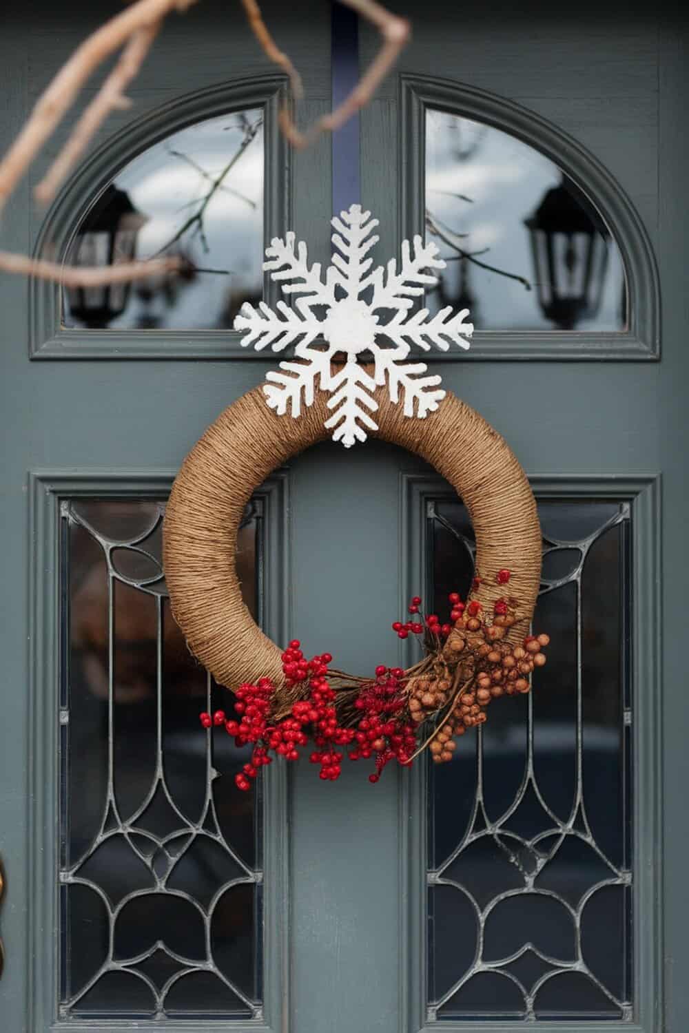 A natural twine wreath decorated with red berries and a white snowflake ornament, hanging on a door.