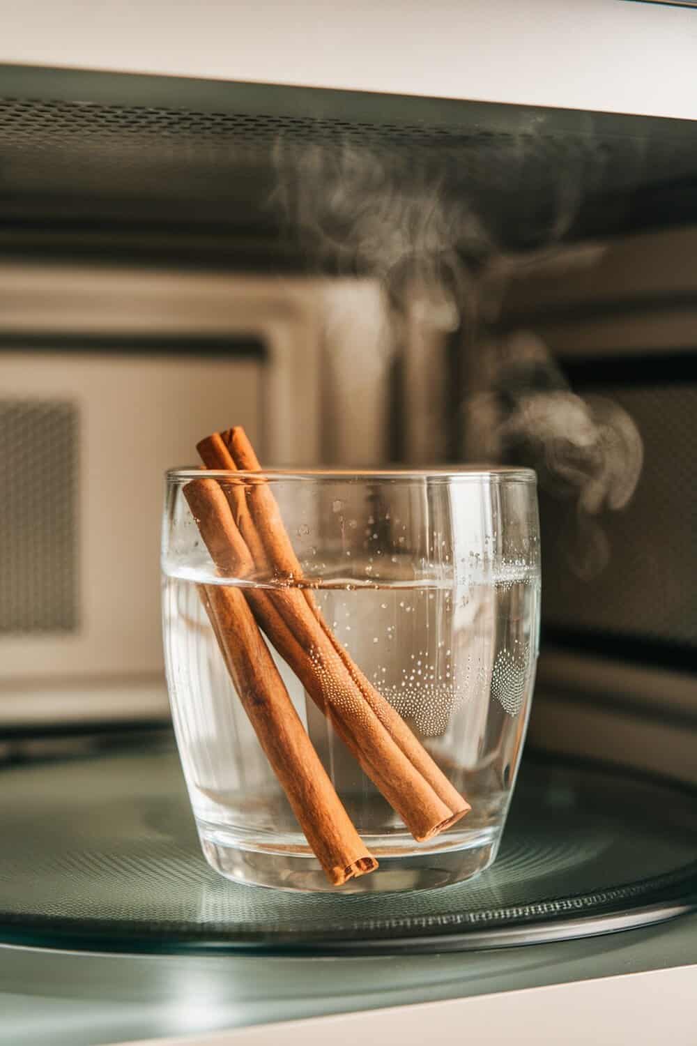 A glass bowl with water and cinnamon sticks inside a microwave, steam rising.