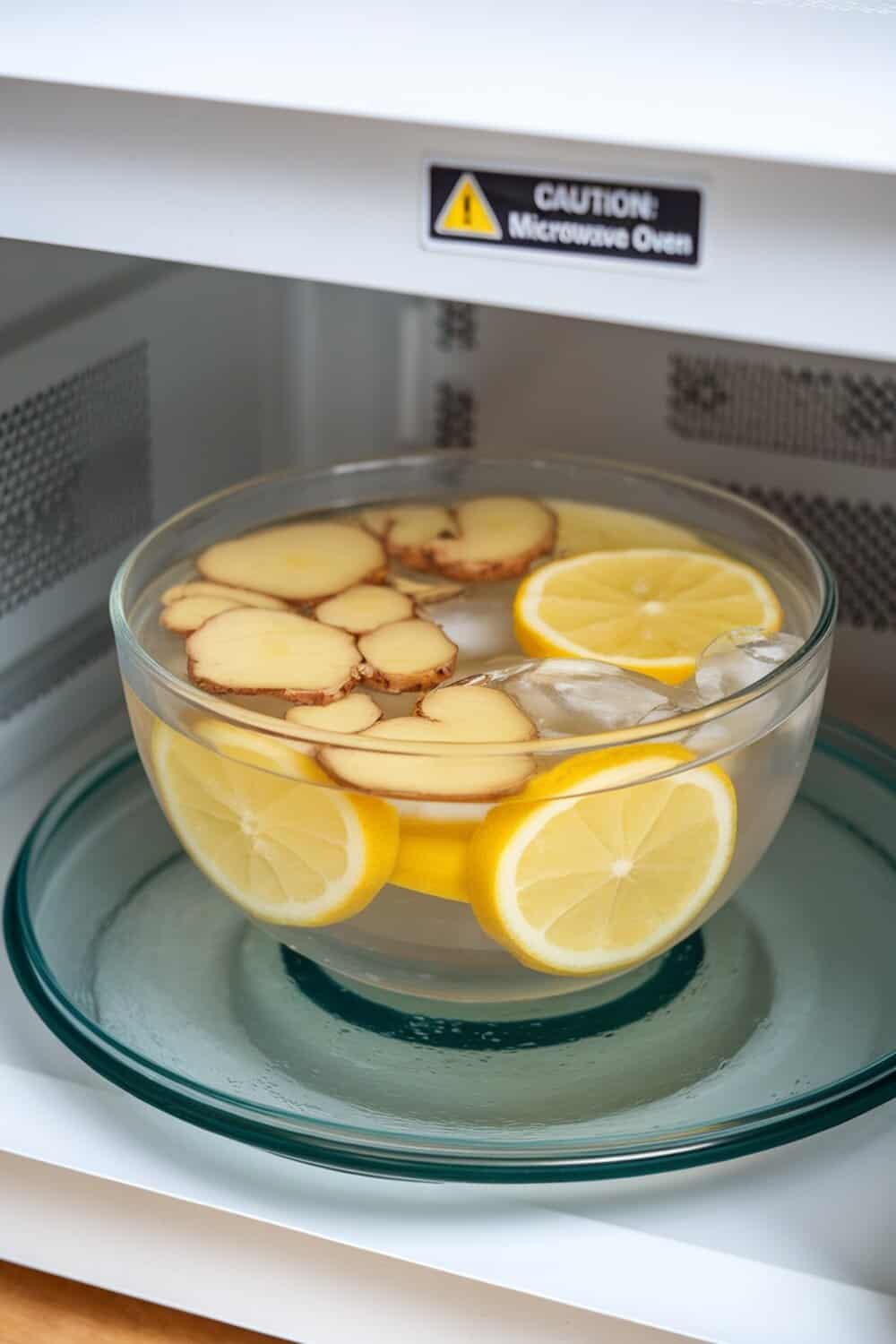 A bowl of water with ginger and lemon slices inside a microwave.