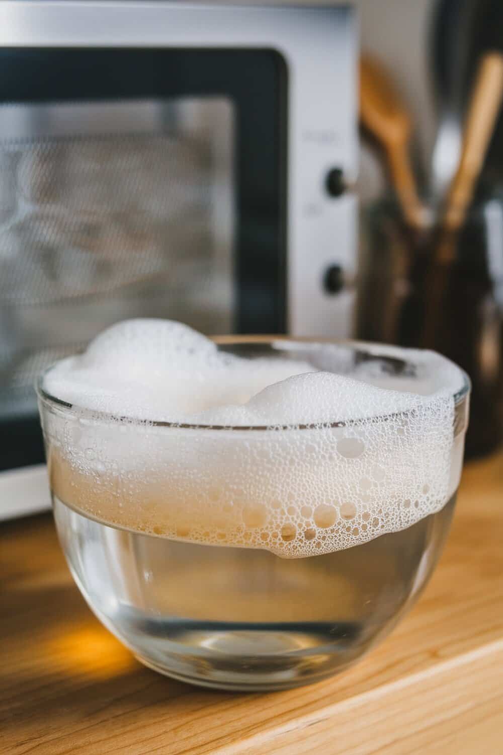 A bowl of foaming soap and vinegar cleaner next to a microwave.