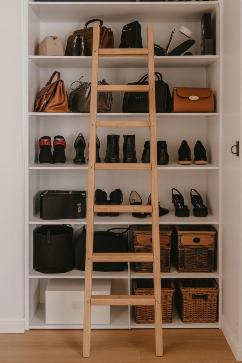 A wooden ladder leaning against a closet shelf filled with bags and shoes.