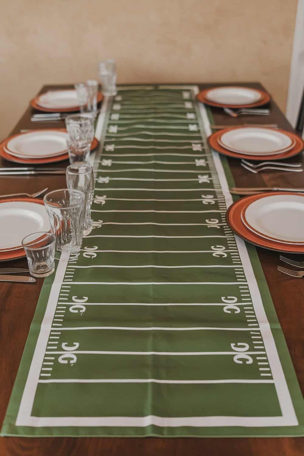 A table set with a football field runner, plates, and glasses.