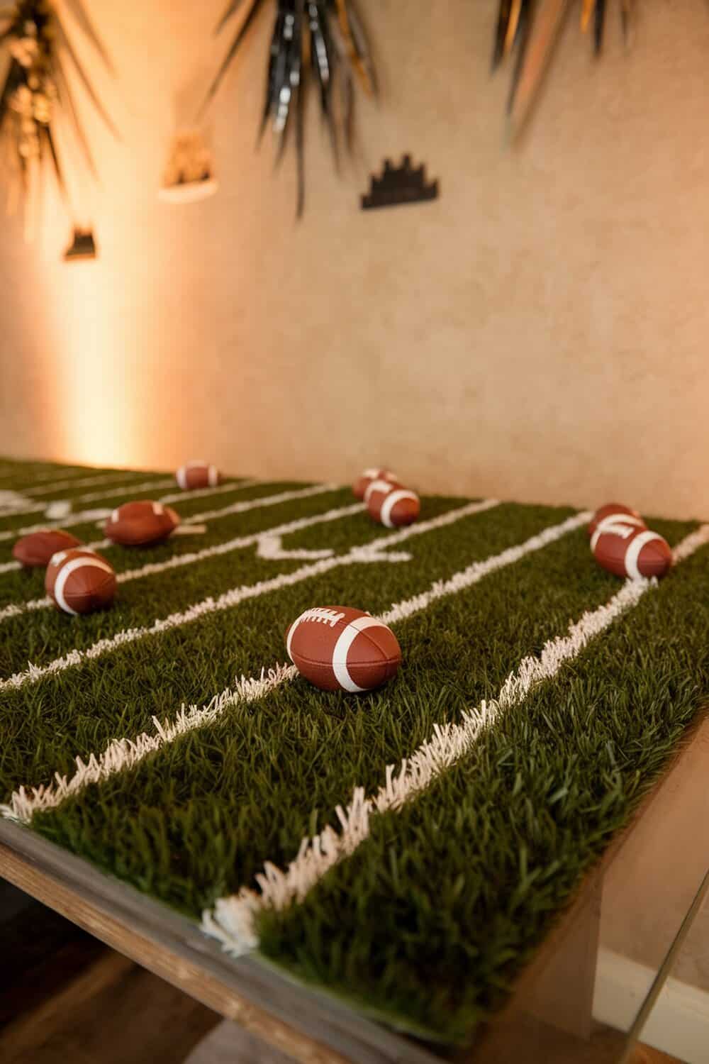 Table decorated with turf grass and mini footballs for a football party.