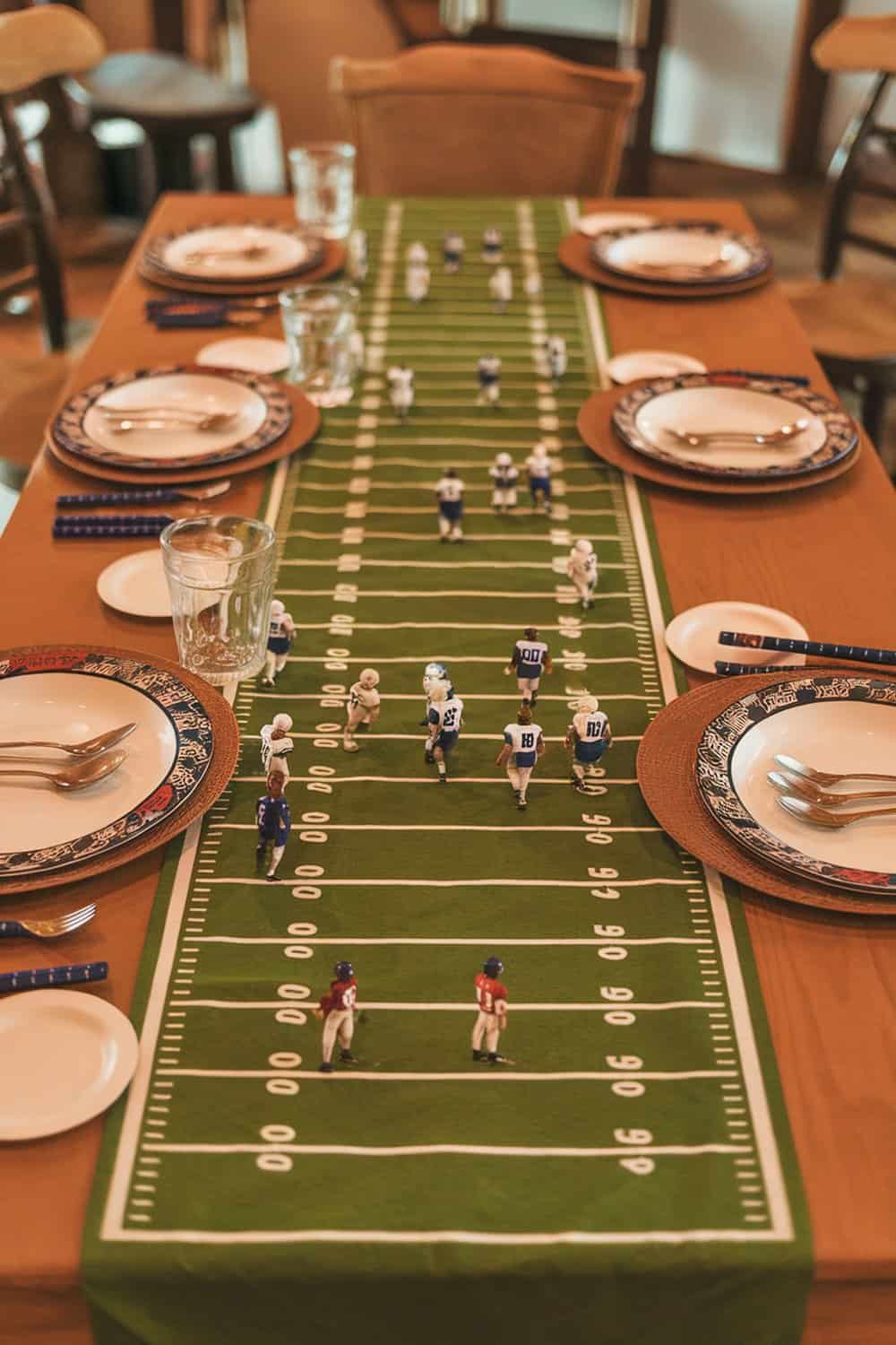 A table set with a green football field table runner, plates, and mini football player figurines.