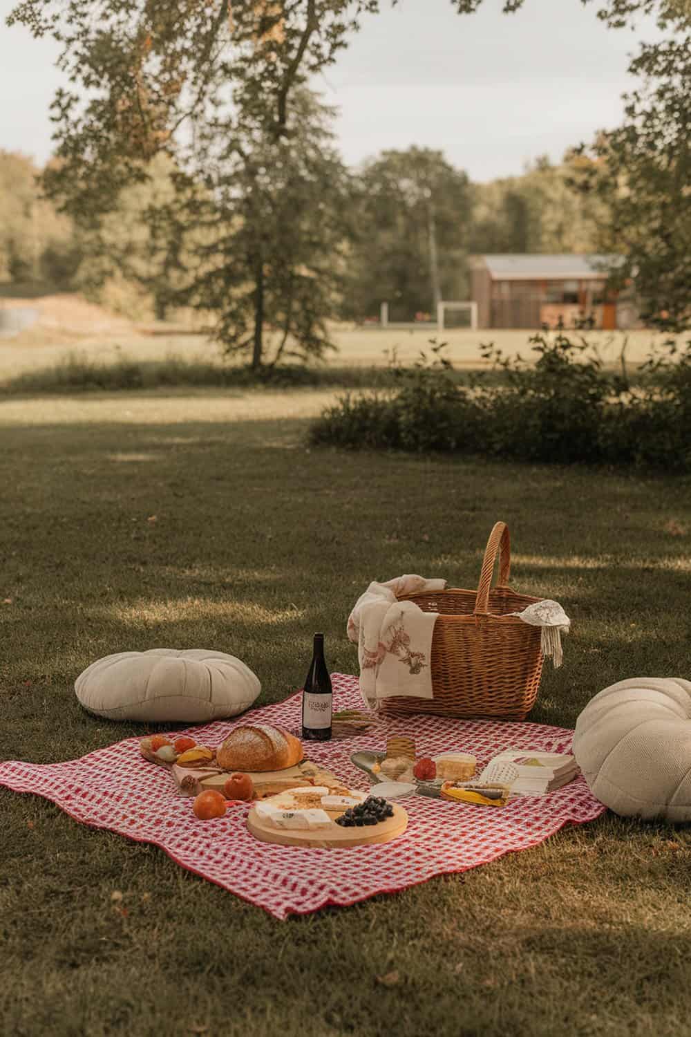 A romantic outdoor picnic setup with a blanket, cushions, and a basket filled with snacks and drinks.