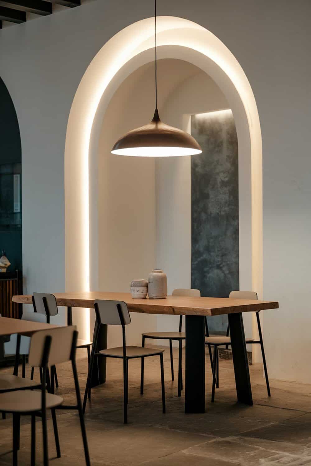 A modern dining area with a stylish pendant light hanging above a wooden table and minimalist chairs.