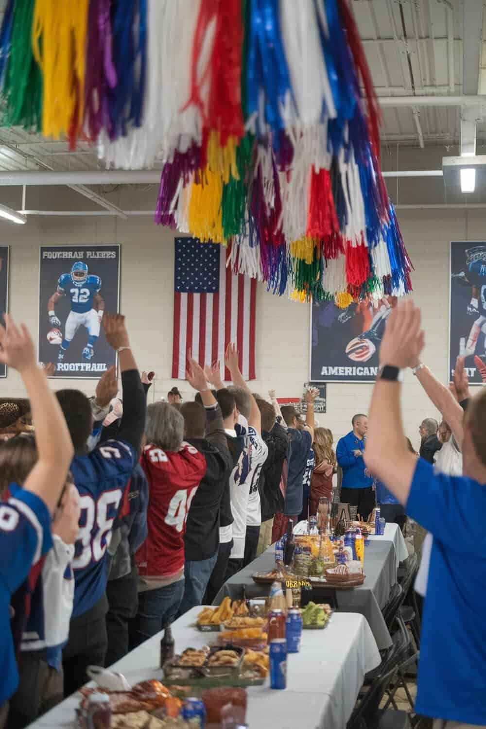 Colorful cheerleader pom-poms hanging from the ceiling at a football party.