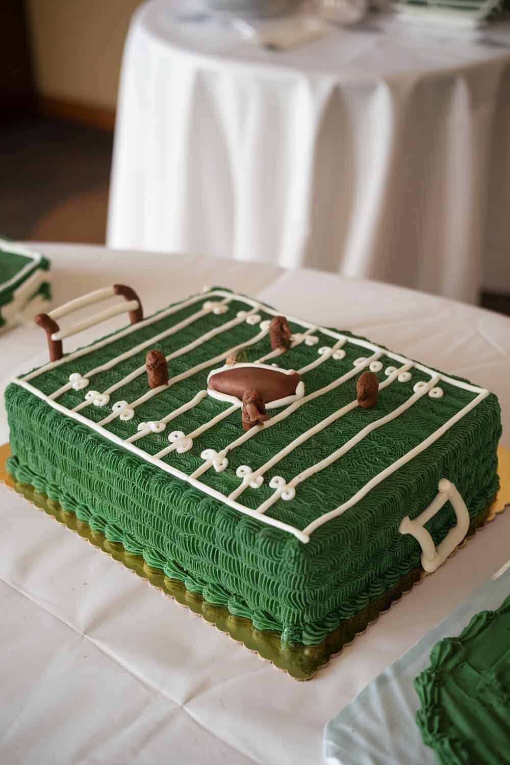 A football field themed cake decorated with green icing, white lines, and chocolate figures.