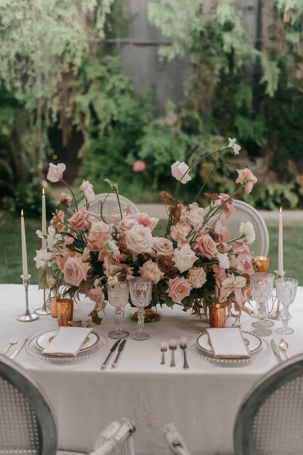 A beautifully arranged floral centerpiece with pink and white flowers, candles, and elegant table settings.