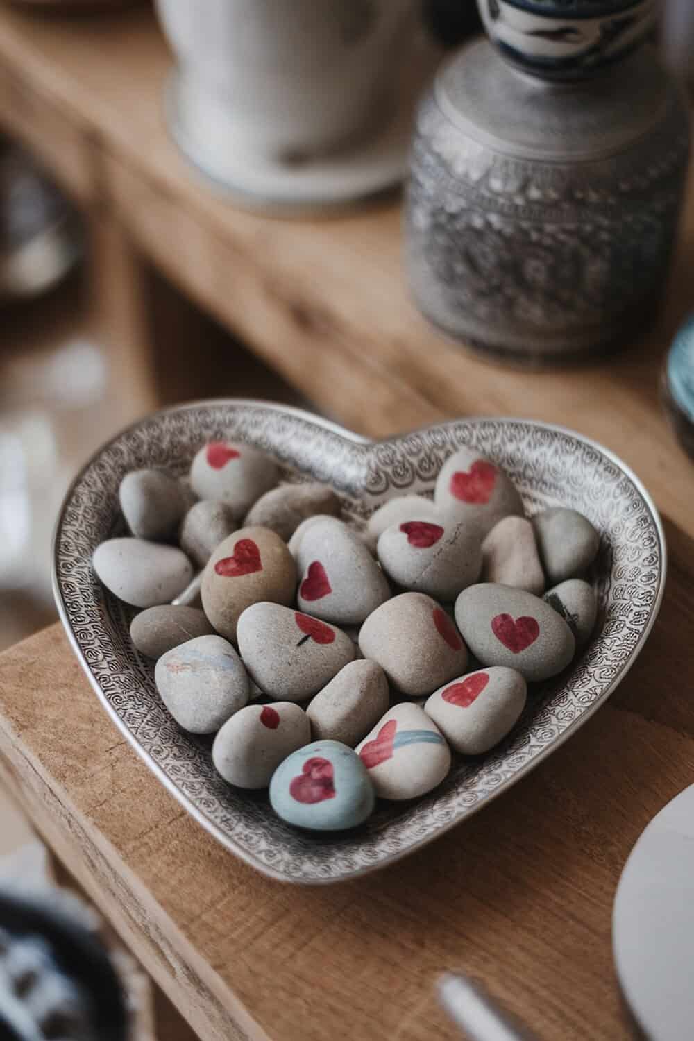 A heart-shaped dish filled with painted stones featuring red hearts.