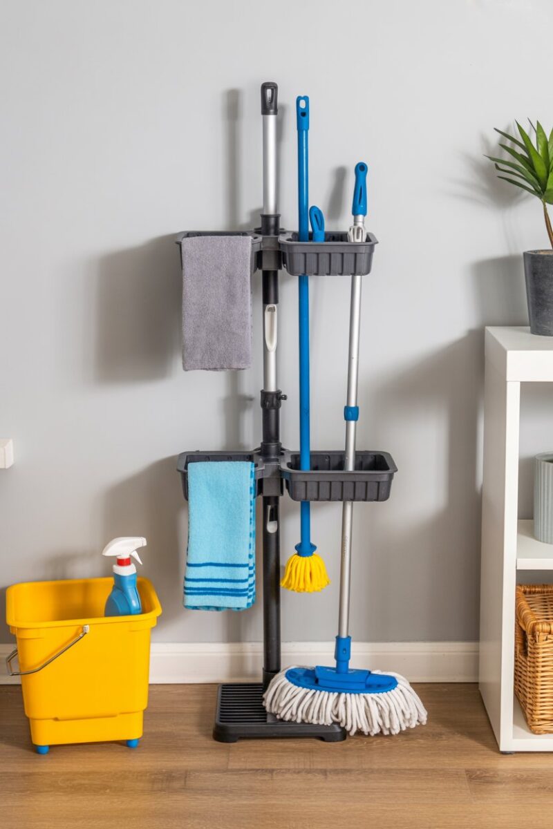 Vertical mop organizer stand holding various cleaning tools.